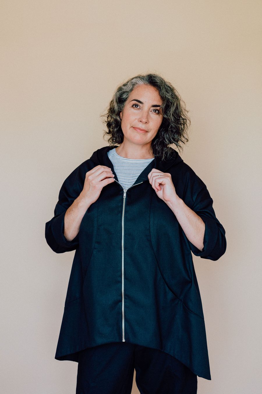 Woman wearing the Hove Jacket pattern from In the Folds on The Fold Line. A jacket pattern made in cotton twill/drill, linen, linen blends or denim fabrics, featuring a loose fit, dropped shoulders, fully lined hood, open-ended zip closure, high-low hem, 