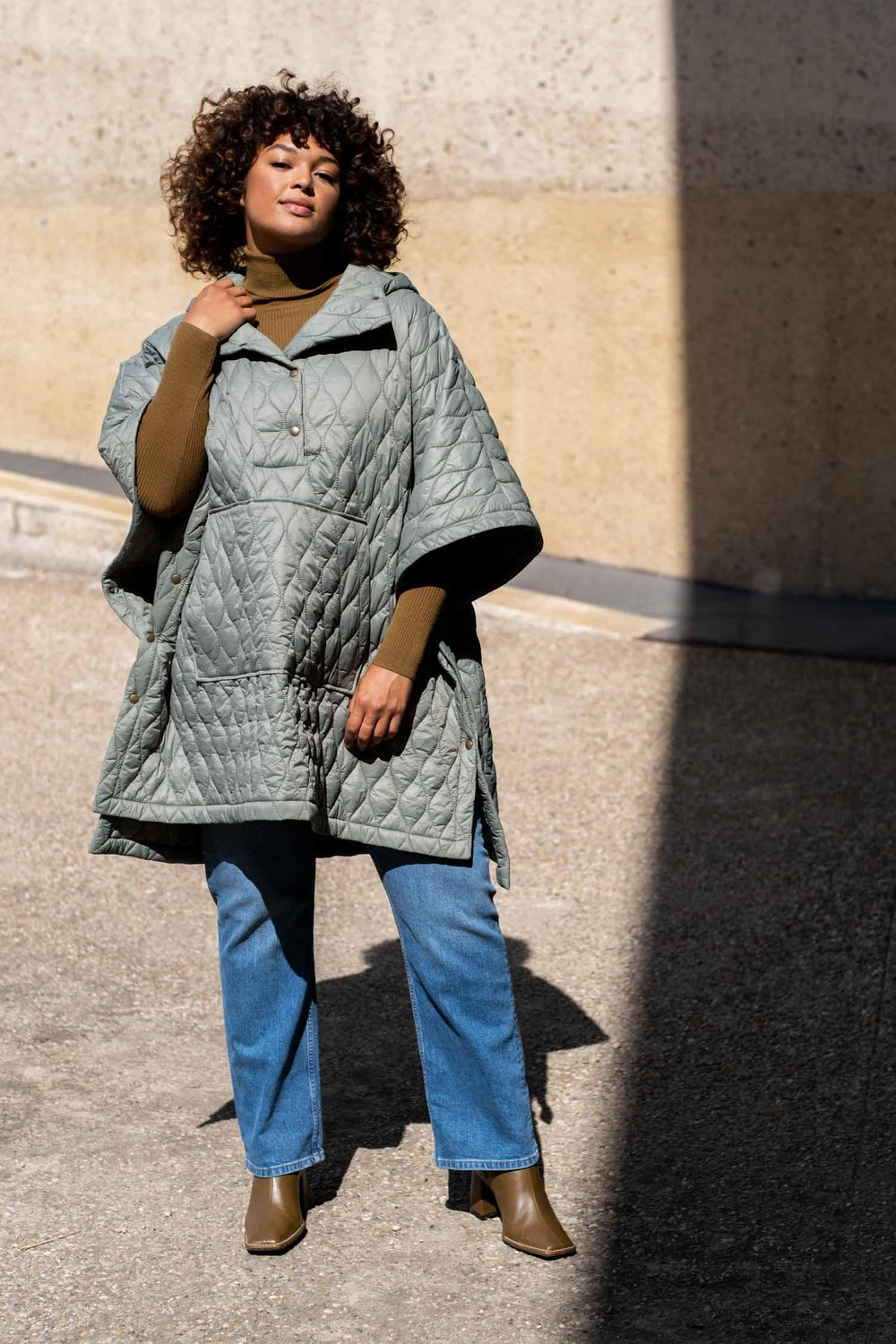 Woman wearing the Harlem Cape sewing pattern from Fibre Mood on The Fold Line. A poncho pattern made in nylon, cotton twill, wool, quilted, padded or matelassé fabrics, featuring a relaxed fit, kangaroo pocket, front and side snap fasteners, hood, high-lo