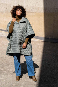 Woman wearing the Harlem Cape sewing pattern from Fibre Mood on The Fold Line. A poncho pattern made in nylon, cotton twill, wool, quilted, padded or matelassé fabrics, featuring a relaxed fit, kangaroo pocket, front and side snap fasteners, hood, high-lo