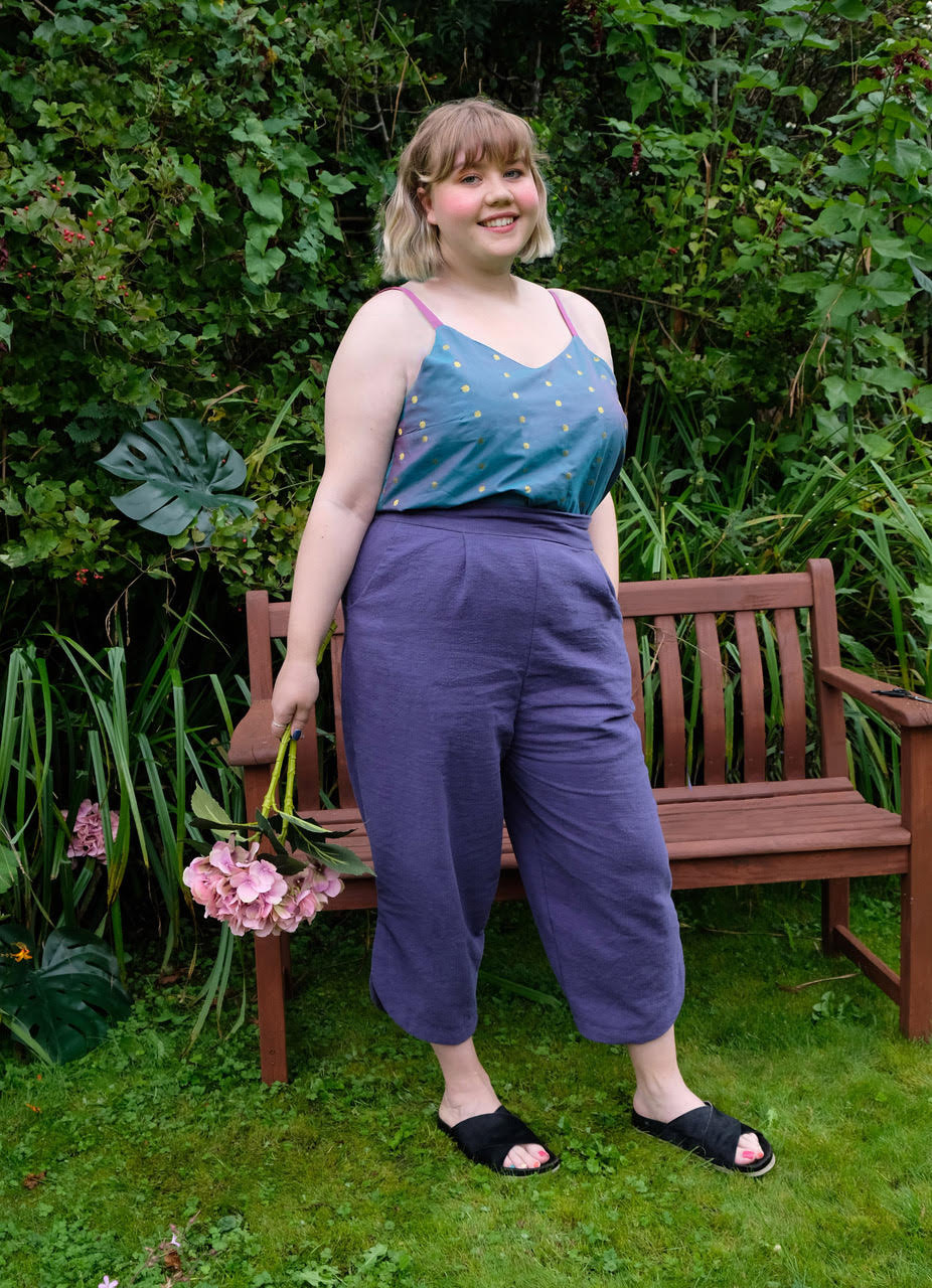 Woman wearing the Harvester Pants sewing pattern from Sew Different on The Fold Line. A trouser pattern made in cotton, linen, denim or needlecord fabrics, featuring a loose fit, 3/4 length trouser, angled pockets, front pleats, scalloped vent at the bott