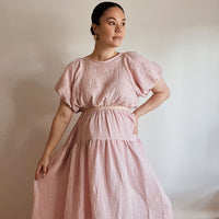 Woman wearing the Hera Dress sewing pattern from Veronica Tucker on The Fold Line. A top and skirt pattern made in linen fabrics, featuring a reversible blouse with tie neck, fully lined puff sleeves, and elasticated waist. The skirt has a curved yoke, po