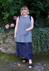 Woman wearing the Herba Apron sewing pattern from Sew Different on The Fold Line. An apron pattern made in cotton, linen, denim or needlecord fabrics, featuring a crossed back design that pulls on over the head, large front pocket, scalloped back hem and 