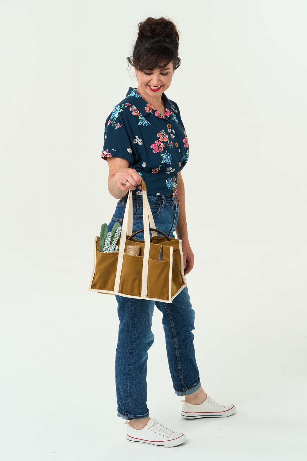 Women holding the Hobby Bag sewing pattern from Sew Over It on The Fold Line. A bag pattern made in cotton twill, cotton drill, canvas or denim fabrics, featuring eight outer pockets, two inner pockets, bound side and bottom edges, and twill tape short ca