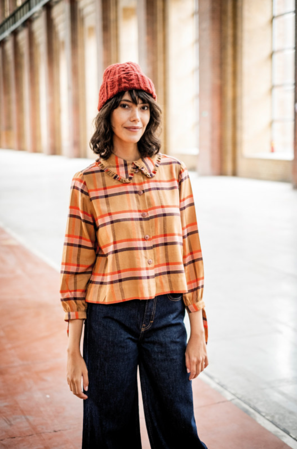 Woman wearing the Honey Top sewing pattern from Fibre Mood on The Fold Line. A top pattern made in Poplin, Tencel, linen, crepe, wools or flannel fabrics, featuring a collar band, ruffled collar trim, back yoke with gathers, boxy fit, button placket, ¾ sl