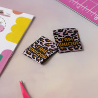 Photo of the 'I Am Unique 2.0' woven labels from Little Rosy Cheeks on The Fold Line. The pack includes 6 woven labels with mustard text on a lilac/pink and black leopard background, ready to be sewn into your handmade clothes.