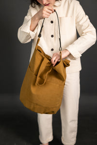 Woman holding The Jack Tar Bag sewing pattern from Merchant & Mills on The Fold Line. A tote bag pattern made in oilskin, sturdy canvas, cotton drill or denim fabrics, featuring three internal pockets, fully lined, fabric handles, leather strap, magnetic 