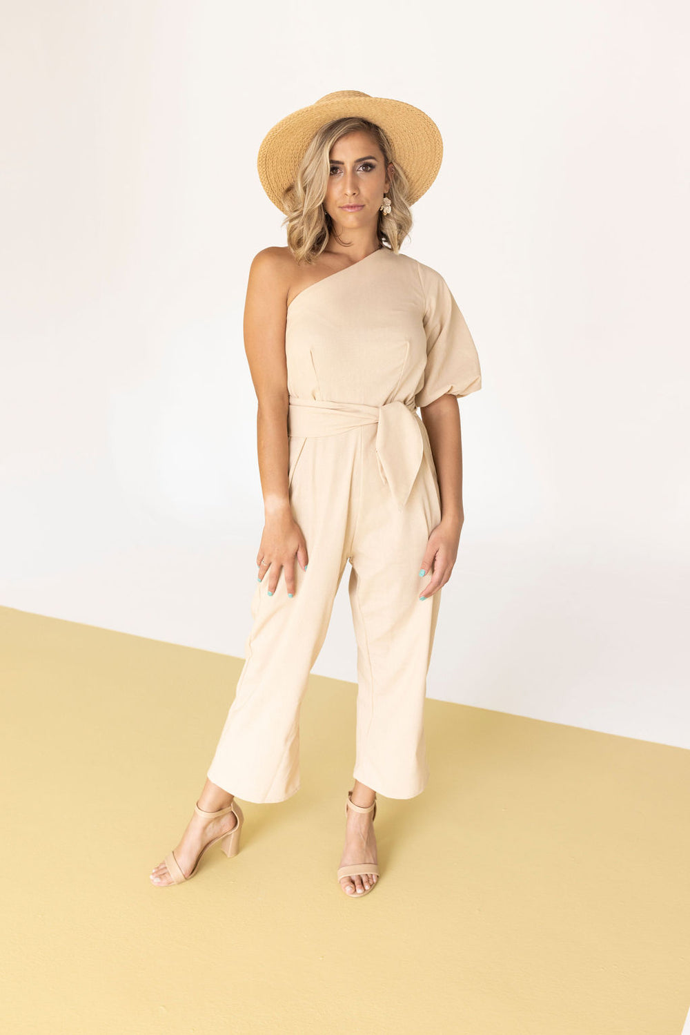 Woman wearing the Jacky Jumpsuit sewing pattern from Pattern Sewciety on The Fold Line. A jumpsuit pattern made in cotton, linen or rayon fabrics, featuring an asymmetrical neckline, cold shoulder, short puff sleeve, front and back waist darts, side invis