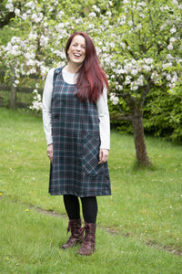 Woman wearing the Jayne Pinafore Dress sewing pattern from Bobbins and Buttons on The Fold Line. A dress pattern made in linen, medium weight denim or medium weight cotton fabrics, featuring an A-line silhouette, no zip, buttons at the shoulders, patch po