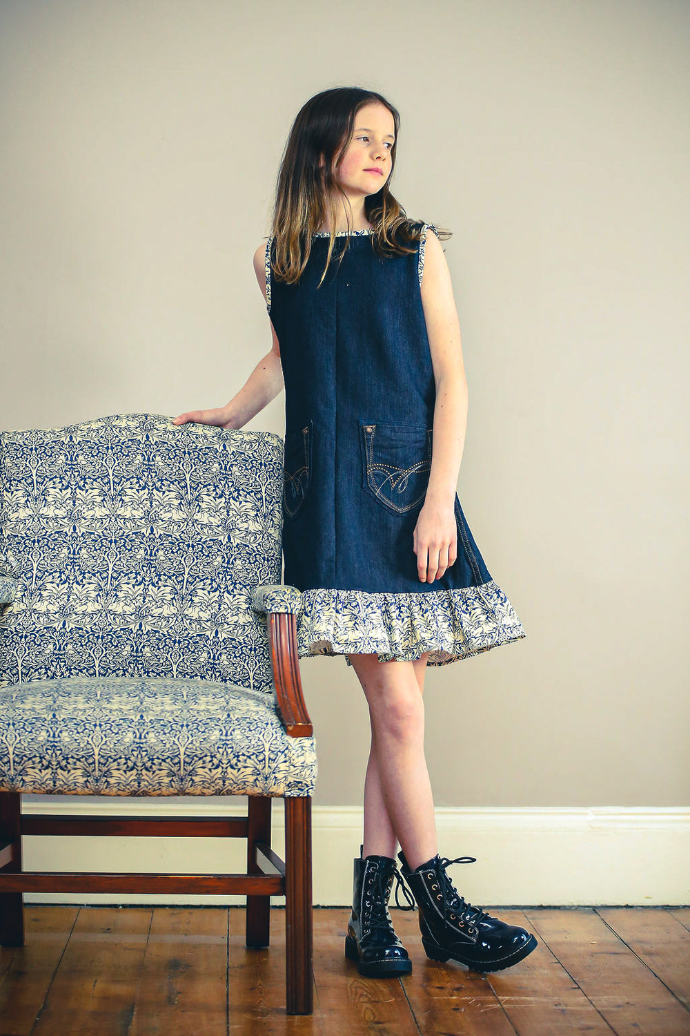 Child wearing the Jeans to Child/Teen Dornoch Dress sewing pattern by Greyfriars and Grace. A sleeveless dress pattern made in pre-loved denim fabrics, featuring an A-line silhouette, front pockets, back zip closure, hem ruffle, and contrasting bias bindi
