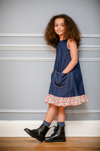 Child wearing the Jeans to Children's Joppa Dress sewing pattern by Greyfriars and Grace. A sleeveless dress pattern made in pre-loved denim fabrics, featuring an A-line silhouette, front pockets, hem ruffle and contrasting bias binding on the neckline, b