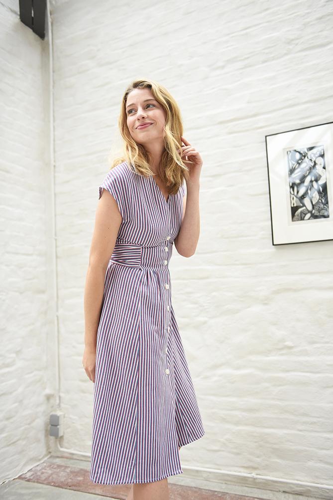 Woman wearing the Joanne Dress sewing pattern from Fibre Mood on The Fold Line. A dress pattern made in cotton twill, denim or cotton satin fabrics, featuring button-front closure, A-line skirt, waist tie at the back, V-neck, grown on cap sleeves and knee