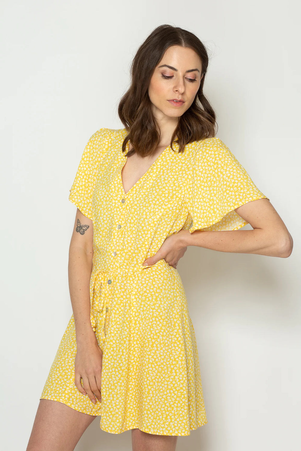 Woman wearing the Julia Dress sewing pattern from Bara Studio on The Fold Line. A dress pattern made in viscose, cotton, linen or Tencel fabrics, featuring a V-neck, button placket, flutter sleeves, mini length, and narrow self-fabric belt.