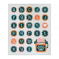 Photo showing the Just My Type Quilt sewing pattern from Pen and Paper Patterns on The Fold Line. A quilt pattern made in quilting cotton fabrics, featuring typewriter and letter blocks. Cutting and assembly instructions are included, making it easy to cu