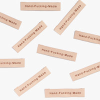 Photo showing 'Hand-Fucking-Made' Woven Labels from Kylie & The Machine on The Fold Line. A washable, durable and non-scratchy fabric label featuring the words 'Hand-Fucking-Made' all ready to be sewn into your handmade clothes.