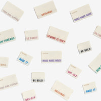 Photo showing numerous woven labels, with a unique word or phrase on each Woven Label from Kylie & The Machine on The Fold Line. A washable, durable and non-scratchy fabric label all ready to be sewn into your handmade clothes.