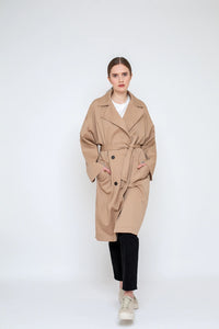 Woman wearing the Kara Trench Coat sewing pattern from Bara Studio on The Fold Line. A trench coat pattern made in cotton, linen or tencel fabrics, featuring an oversized fit, loose drape, dropped shoulders, front button closure, front pockets, tie belt, 