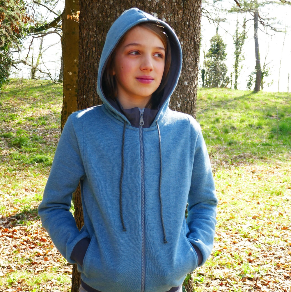 Child wearing the Child/Teen Keefe Sweatshirt sewing pattern from Petits D’om on The Fold Line. A hoodie pattern made in sweatshirt fabric such as brushed, fleece, jogging fabric or French terry fabrics, featuring centre front zip closure, full length sle