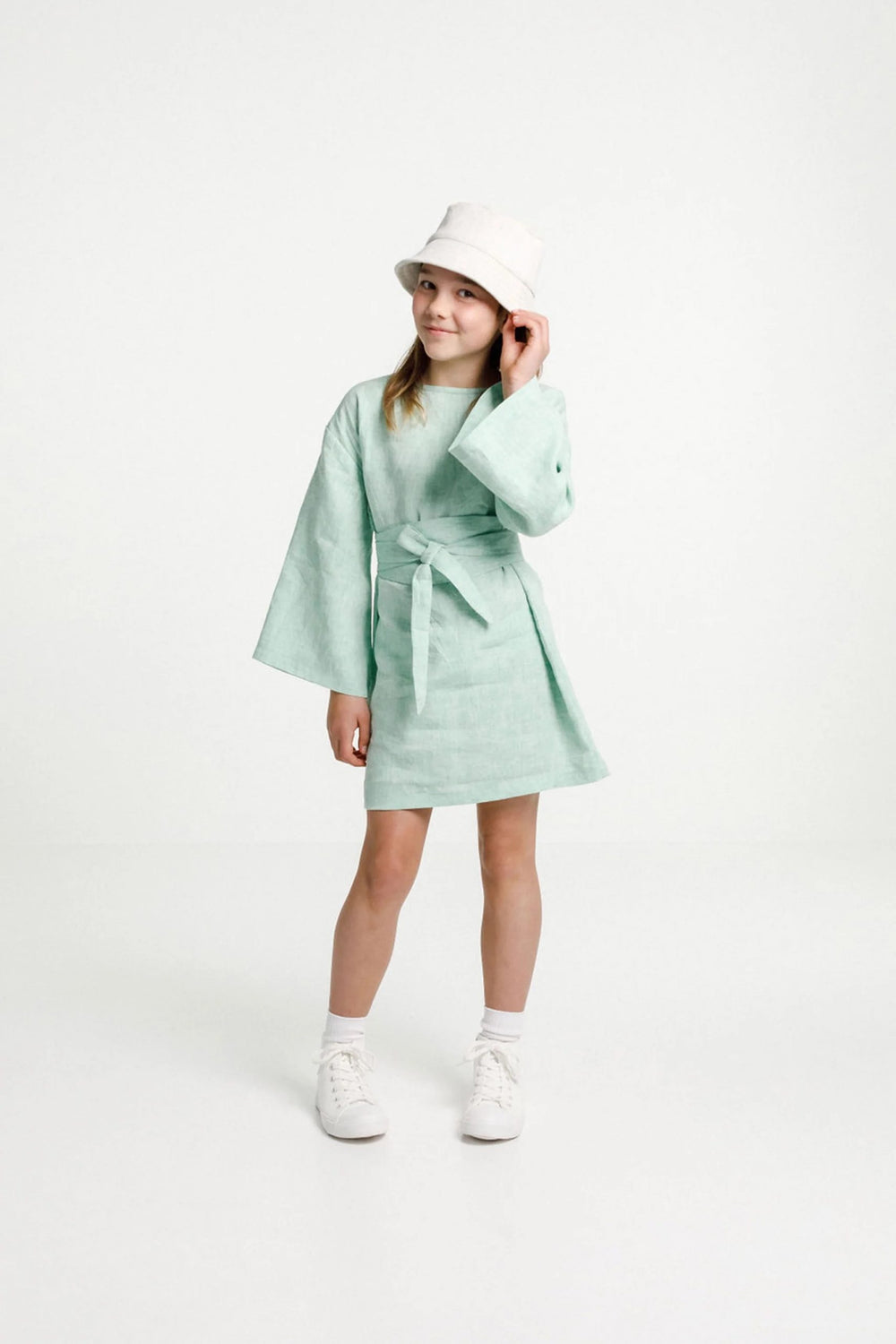 Child wearing the Array Dress sewing pattern from Papercut Patterns on The Fold Line. A dress pattern made in cotton, linen, rayon or medium weight jersey fabrics, featuring wide flared sleeves, straight-cut body, extra-long wrap-around waist ties and sli