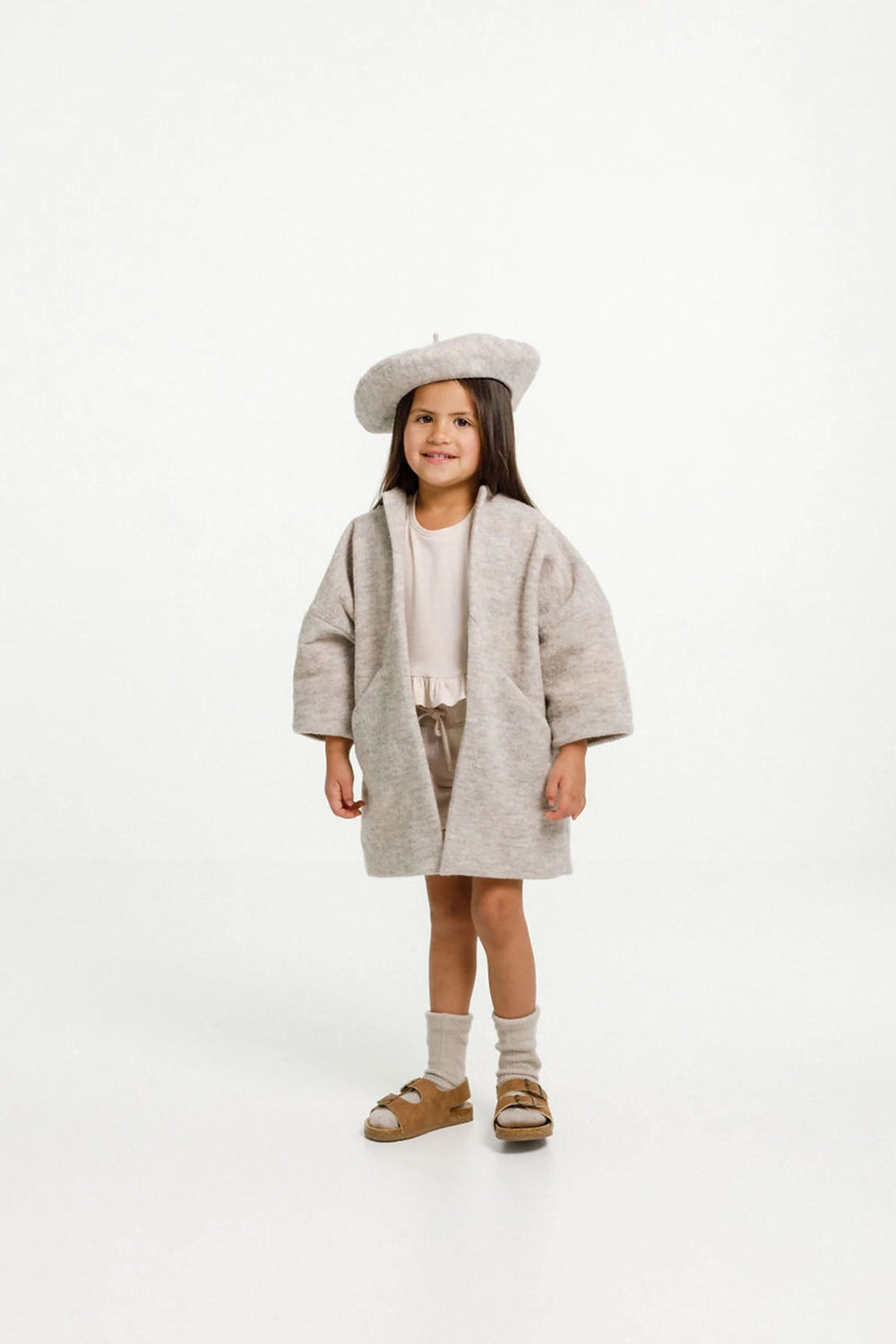 Child wearing the Nova Coat sewing pattern from Papercut Patterns on The Fold Line. A dress pattern made in light cotton, linen, rayon or heavy wool fabrics, featuring angled seaming with hidden pockets, long sleeves, full length, relaxed fit and fully li