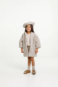 Child wearing the Nova Coat sewing pattern from Papercut Patterns on The Fold Line. A dress pattern made in light cotton, linen, rayon or heavy wool fabrics, featuring angled seaming with hidden pockets, long sleeves, full length, relaxed fit and fully li