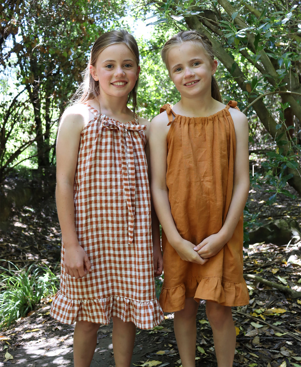 Children wearing the Baby/Child Kororā Dress sewing pattern by Below the Kowhai. A sleeveless dress pattern made in light to medium weight cotton, chambray, lawn, linen, rayon, viscose or voile fabrics, featuring a halter neck and shoulder ties, plus a ru