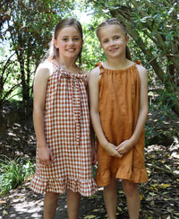 Children wearing the Baby/Child Kororā Dress sewing pattern by Below the Kowhai. A sleeveless dress pattern made in light to medium weight cotton, chambray, lawn, linen, rayon, viscose or voile fabrics, featuring a halter neck and shoulder ties, plus a ru