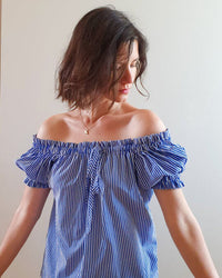 Woman wearing the Polaris Top sewing pattern by French Poetry. A top pattern made in cotton lawn, shirting, viscose, silk crepe, twill or challis fabrics, featuring an off-the-shoulder peasant top with gathers on the neckline and arms, the gathers are mad