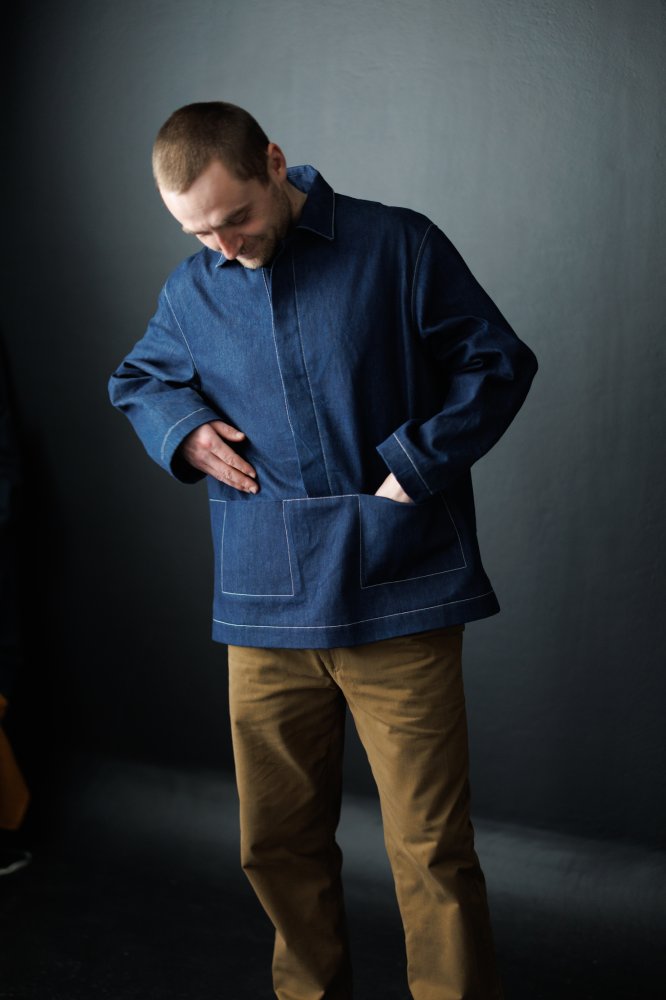 Man wearing the Unisex Ludlow Top sewing pattern from Merchant & Mills on The Fold Line. A top pattern made in cotton canvas and twill, dry oilskin, oilskin, denim and corduroy fabrics, featuring a pull-over smock style, integrated pockets, collar, concea