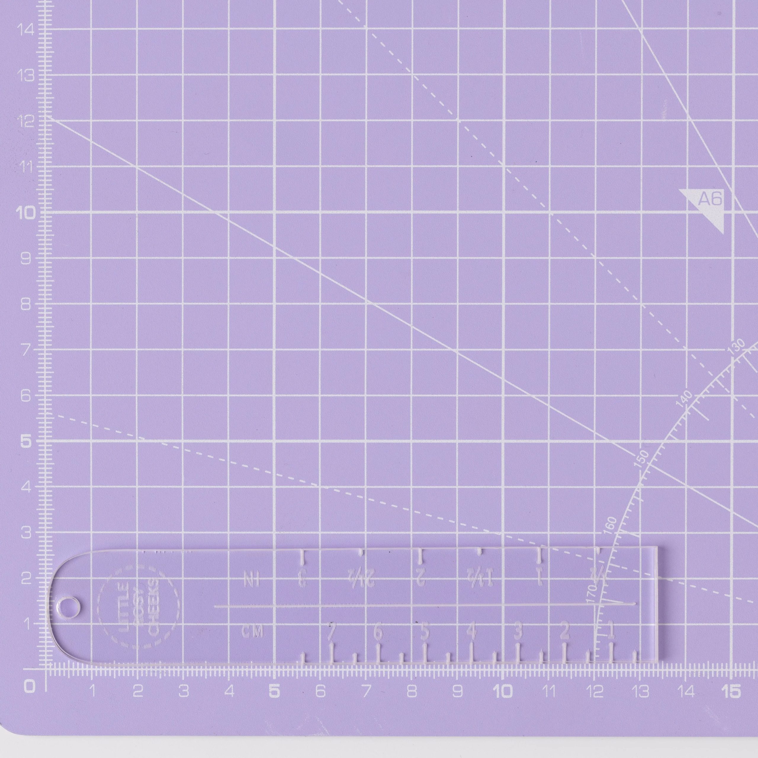 Photo of the Label Placement Ruler from Little Rosy Cheeks on The Fold Line. A transparent acrylic ruler marked in centimetres and inches to achieve sewing label placement perfection.