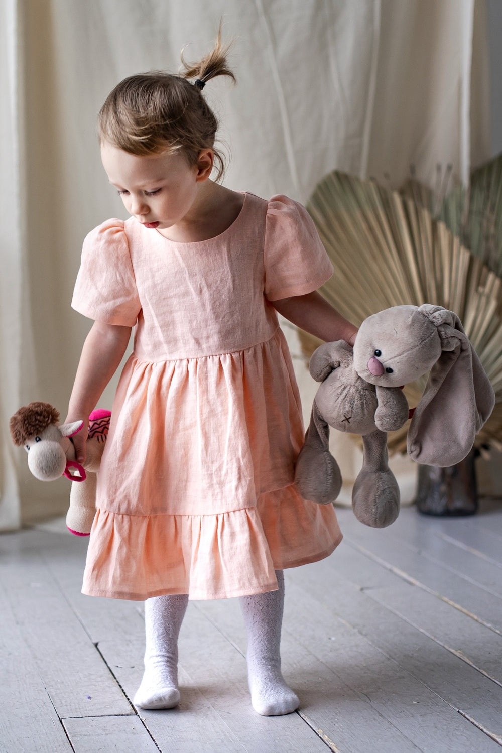 Child wearing the Children's Little Naya Dress sewing pattern from Kate’s Sewing Patterns on The Fold Line. A dress pattern made in cotton or linen fabrics, featuring a high waistline, voluminous sleeves with shoulder gathers, gathered skirt with hem ruff