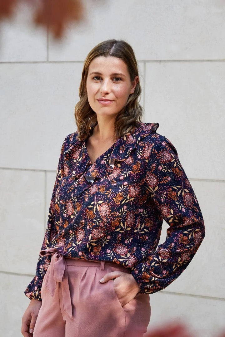 Woman wearing the Liv Blouse sewing pattern from Atelier Jupe on The Fold Line. A blouse pattern made in viscose or tencel fabrics, featuring a loose-fit, V-neckline, ruffle at the front neckline, back yoke with gathers and long sleeves with elasticated h