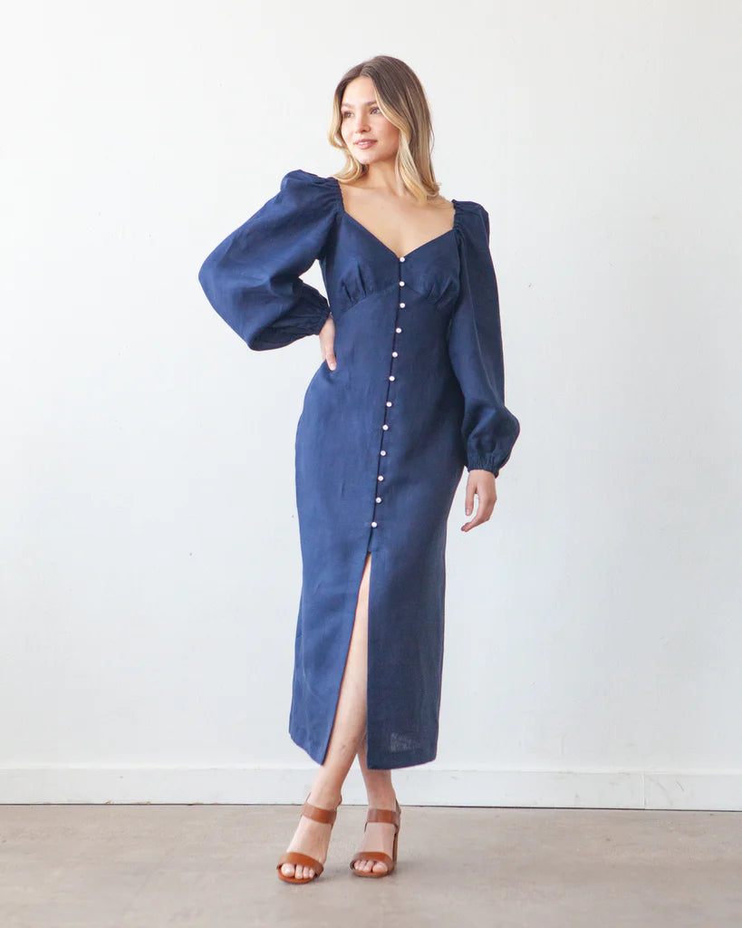 Woman wearing the Lora Dress sewing pattern from True Bias on The Fold Line. A dress pattern made in linen, cotton or rayon fabrics, featuring an empire waist, underbust gathers, low neckline, button and loop centre front closure, long puff sleeves, fitte