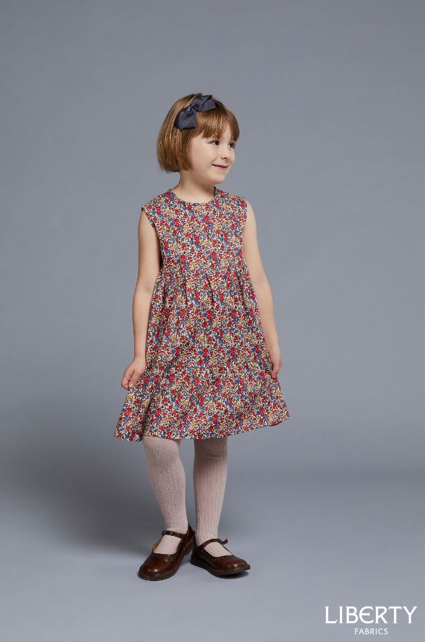 Child wearing the Baby/Child Mabel Tiered Dress sewing pattern by Liberty Sewing Patterns. A sleeveless dress pattern made in cotton or linen fabrics, featuring a gathered tiered dress, back zipper closure and jewel neckline.