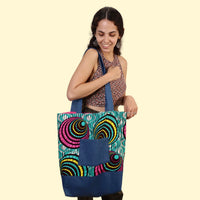 Woman holding the Madeline Tote Bag sewing pattern from Sirena Patterns on The Fold Line. A lined tote bag pattern made in novelty cotton, cotton blends or denim fabrics, featuring an oversized silhouette, patch pocket, shoulder straps and no closures.