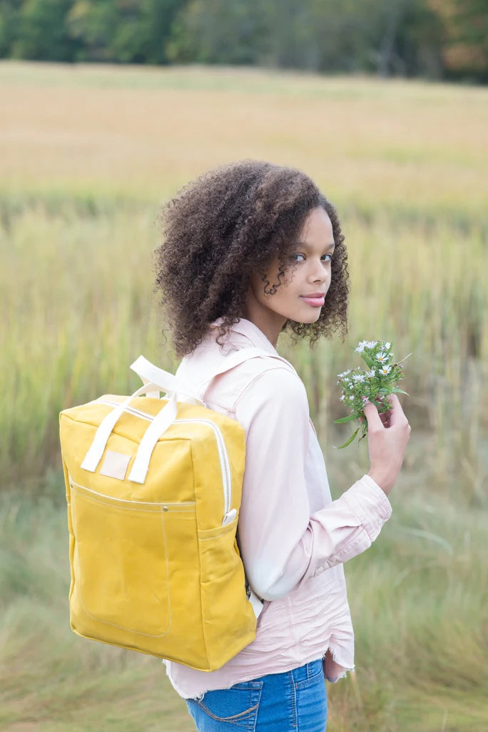 Woman wearing the Making Backpack sewing pattern from Noodlehead on The Fold Line. A backpack pattern made in canvas or waxed canvas fabrics, featuring a rectangular shape, 2 side pockets, back pocket, top zip closure, internal zipped pocket, short carry 