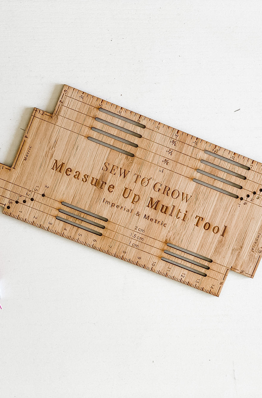 Photo showing the Measure Up Multi Tool from Sew to Grow on The Fold Line. A sewing tool cut from premium bamboo and engraved with imperial and metric markings so you can easily measure and mark your sewing projects.