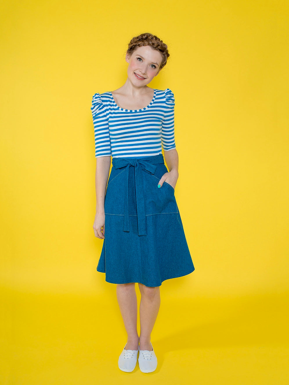 Woman wearing the Miette Skirt sewing pattern from Tilly and the Buttons on The Fold Line. A wrap skirt pattern made in denim, linen, or cotton fabric, featuring a gently flared shape, ties that wrap around and tie at the front in a bow, patch pockets, an