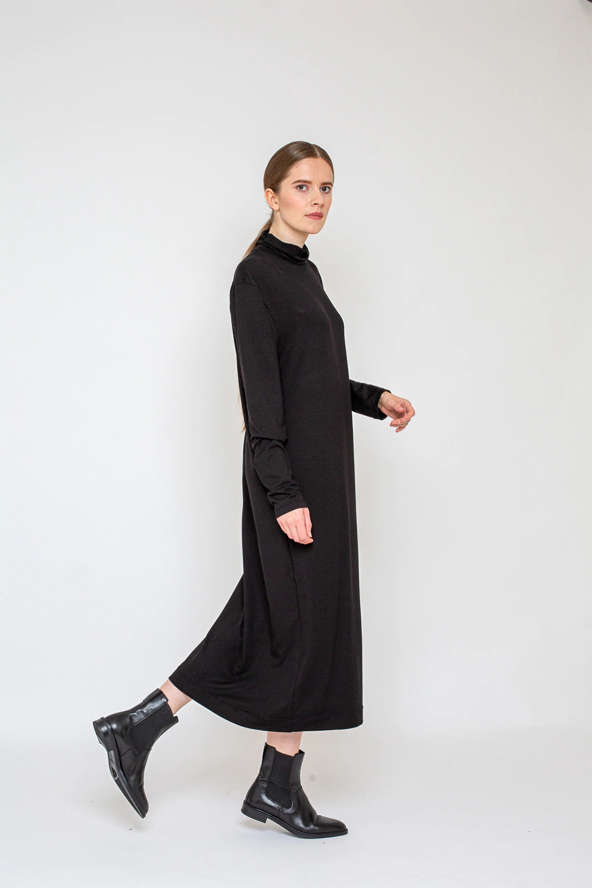 Woman wearing the Mila Dress sewing pattern from Bara Studio on The Fold Line. A dress pattern made in jersey, interlock or punta di roma fabrics, featuring a relaxed fit, turtleneck, longer than normal sleeves and midi length hem.