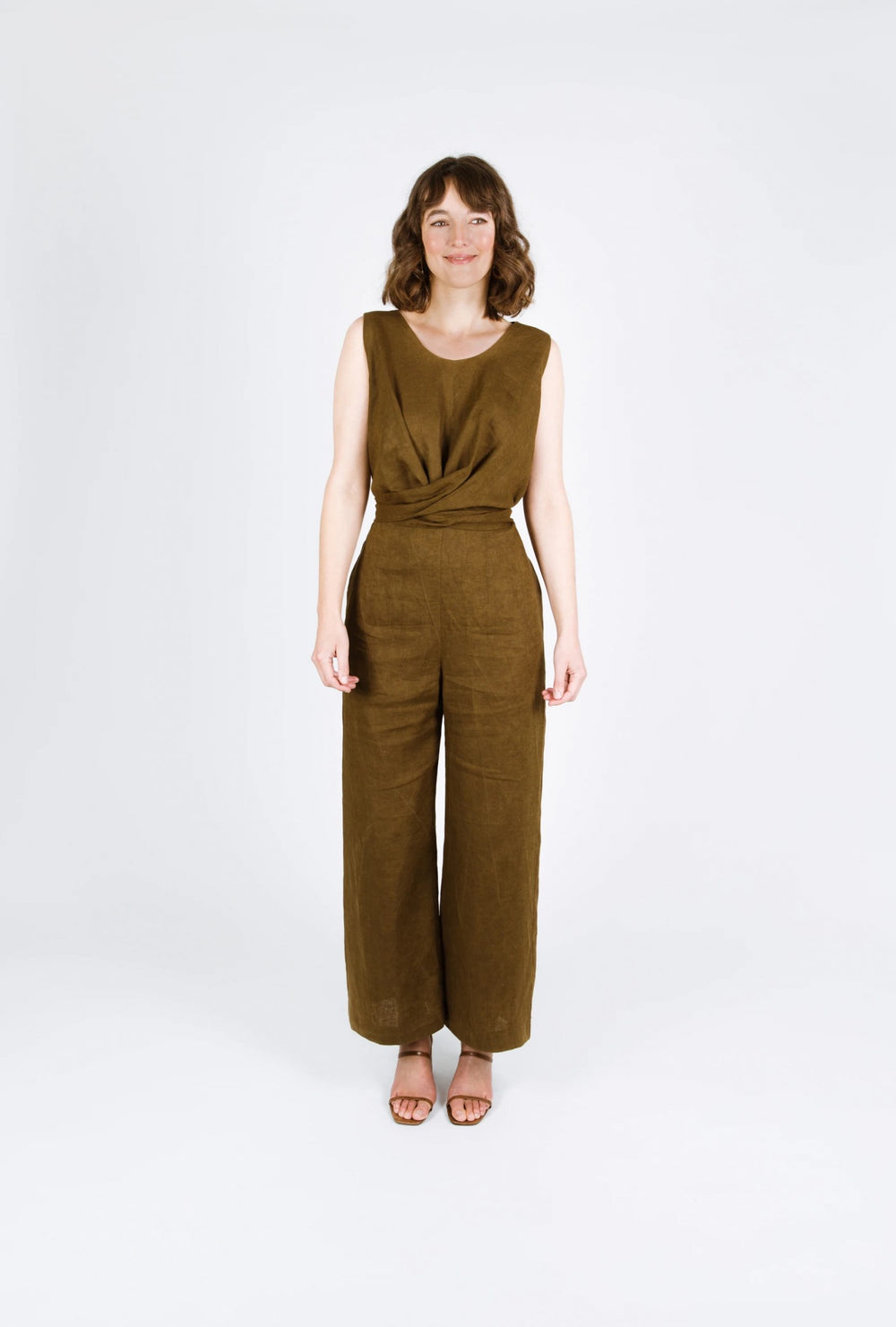 Woman wearing the Mirri Jumpsuit sewing pattern from Papercut Patterns on The Fold Line. A jumpsuit pattern made in cotton, or linen fabrics, featuring a twisted wrap around tie detail, straight legs, scoop neckline, sleeveless, back button-and-loop closu