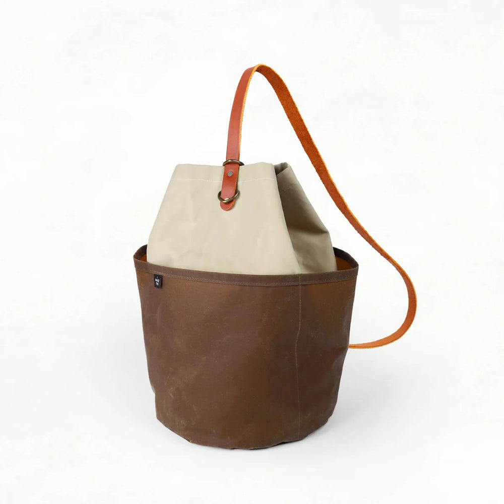 Photo showing the Naito Bucket Bag sewing pattern from Klum House on The Fold Line. A bucket bag pattern made in canvas, waxed canvas, or denim fabrics, featuring a cylindrical body, sit-flat base, interior and exterior pockets, magnetic snap rivet closur