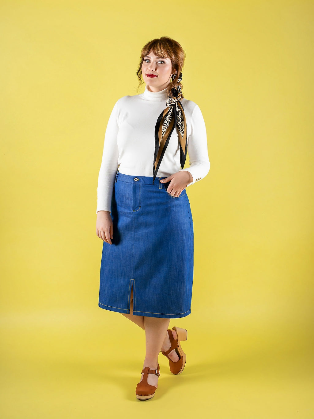 Woman wearing the Ness Skirt sewing pattern from Tilly and the Buttons on The Fold Line. A skirt pattern made in denim, corduroy, jacquard, gobelin (tapestry), drill, or wool fabric, featuring a straight silhouette, shaped waistband, zip fly front, topsti
