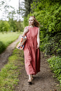 Woman wearing the Nikka Dress sewing pattern from Fibre Mood on The Fold Line. A sleeveless dress pattern made in seersucker, poplin, linen, supple twill, double gauze, and chambray fabrics, featuring a maxi length, gathered tiers, round neckline, bust da