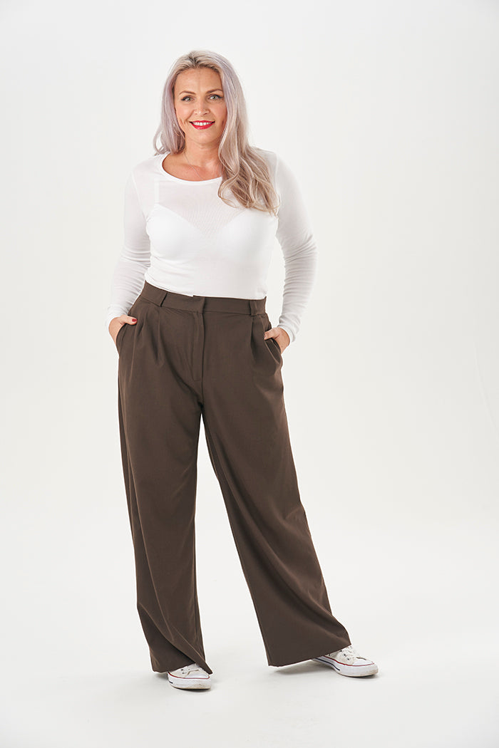 Woman wearing the Nina Trousers sewing pattern from Sew Over It on The Fold Line. A trousers pattern made in crepe and wool suiting fabrics, featuring a wide-leg, high fitted waist, front waist pleats, back double darts, straight waistband, zip fly openin