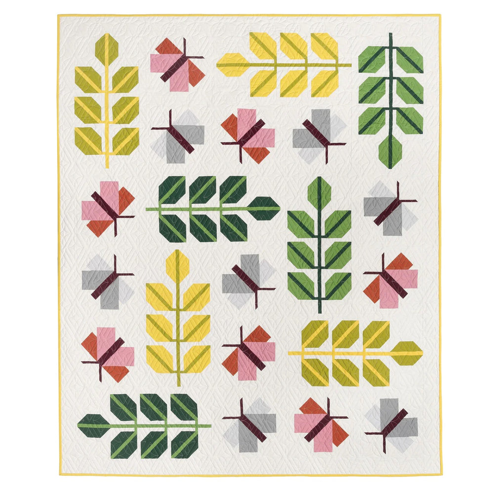 Photo showing the Oak Moth Quilt sewing pattern from Pen and Paper Patterns on The Fold Line. A quilt pattern made in quilting cotton fabrics, featuring multicoloured moths and fern leaves on a pale cream background with instructions for piecing a single 