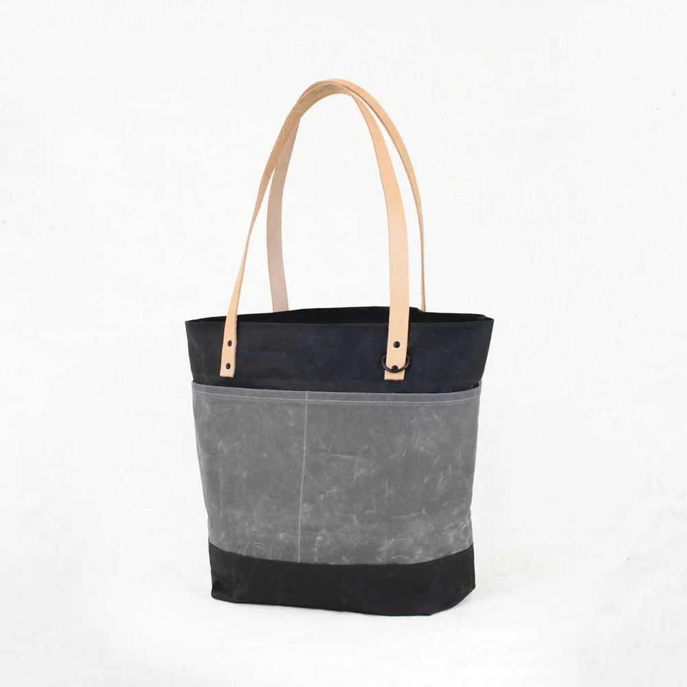 Photo showing the Oberlin Tote Bag sewing pattern from Klum House on The Fold Line. A tote bag pattern made in canvas, waxed canvas, or denim fabrics, featuring leather straps, magnetic snap closure, interior zipper pocket, exterior pocket compartments, a