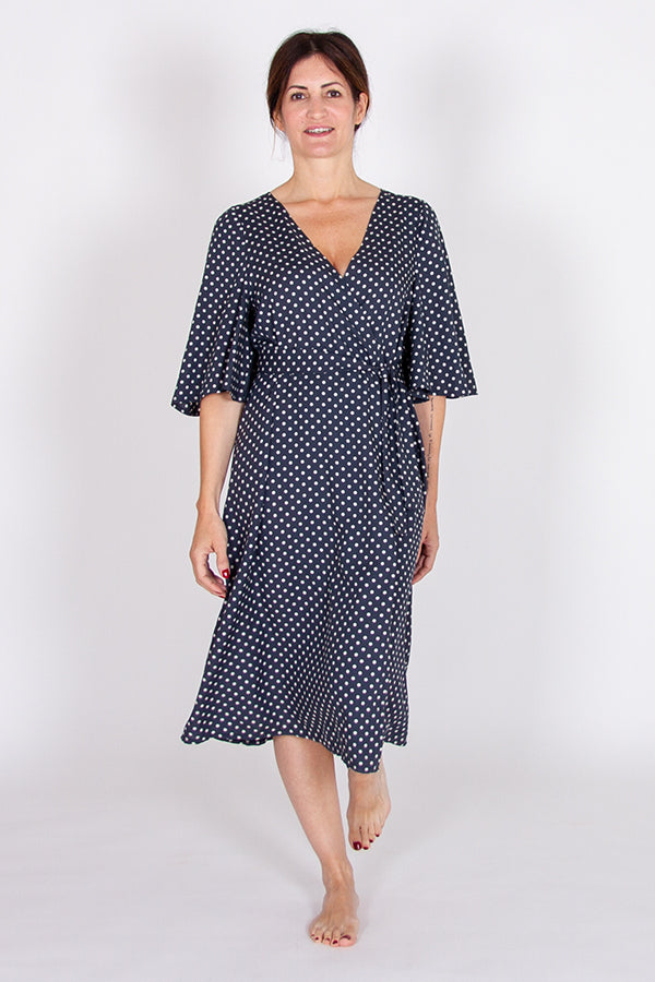 Woman wearing the Octarine Wrap Dress sewing pattern from I AM Patterns on The Fold Line. A wrap dress pattern made in viscose, tencel, crepe, linen or silk fabrics, featuring a V-neck, knee-length, elbow-length butterfly sleeves, waist button closure, be