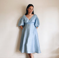 Woman wearing the Odette Dress sewing pattern from Veronica Tucker on The Fold Line. A dress pattern made in linen fabrics, featuring a faux-wrap, V-neck, bias cut, full circle skirt, bodice and sleeve darts, and midi length.