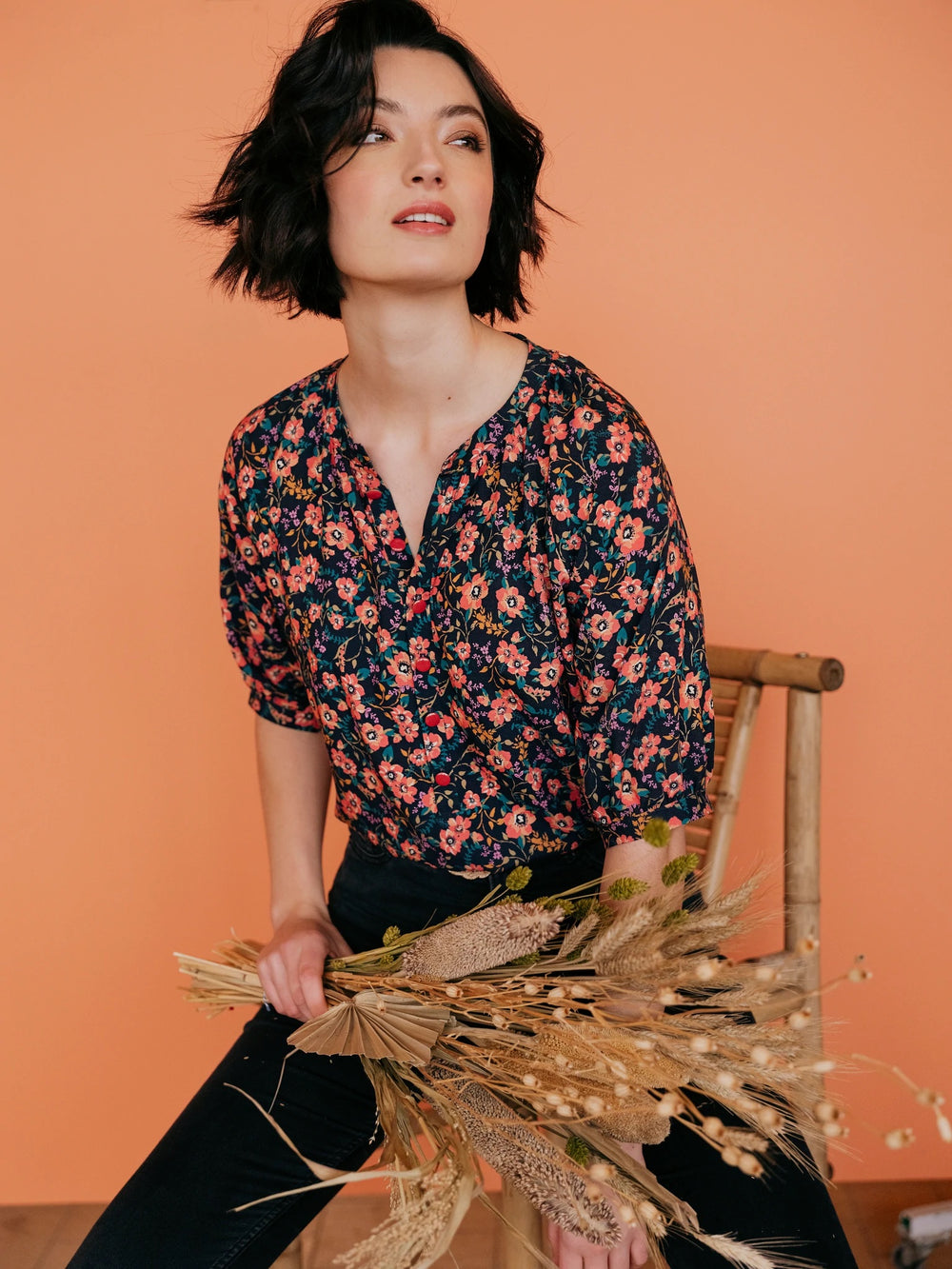 Woman wearing the Olivia Blouse sewing pattern from Atelier Jupe on The Fold Line. A blouse pattern made in viscose, tencel, cotton or linen fabrics, featuring medium length raglan sleeves, gathers at the collar, popover button placket and slightly rounde