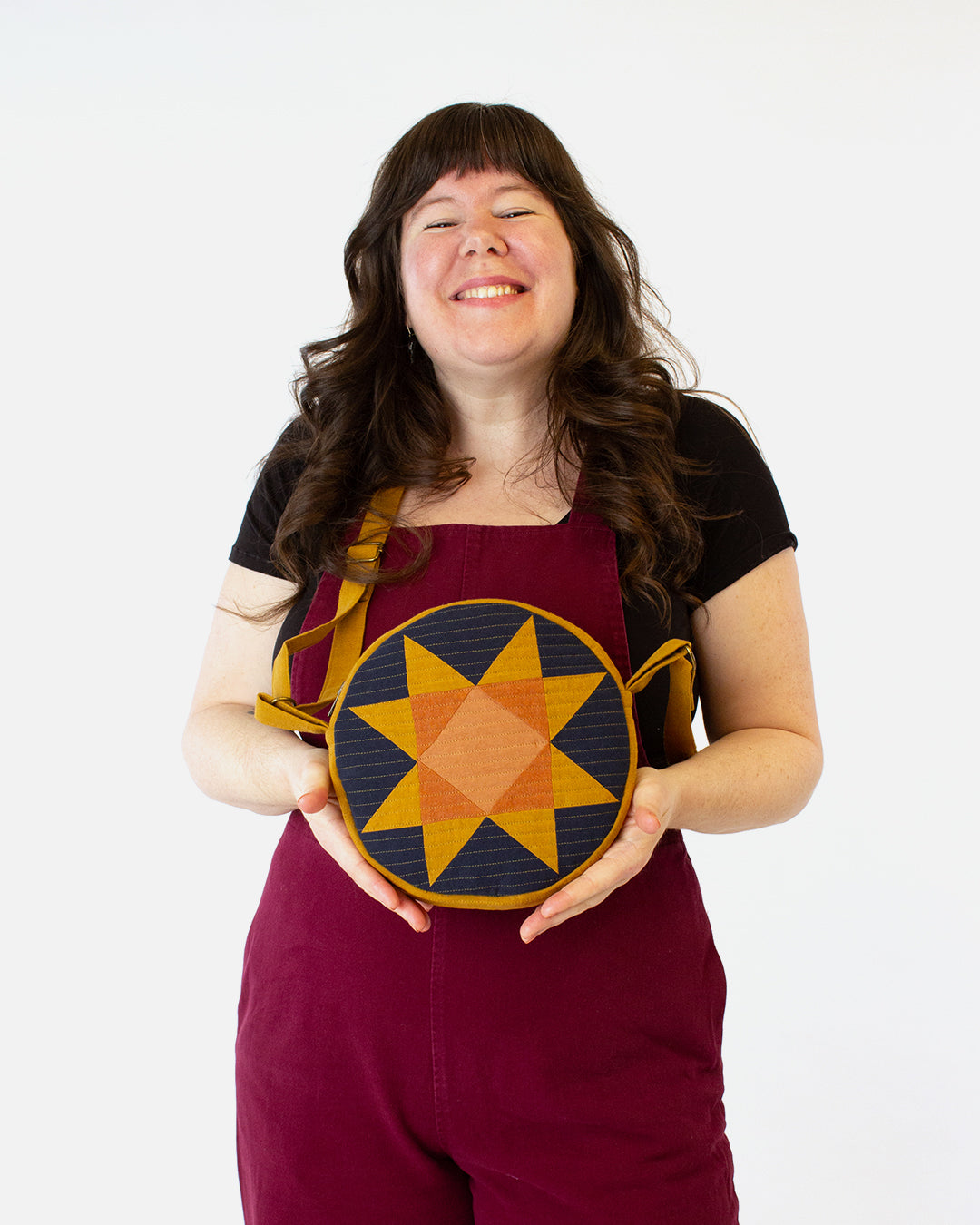 Woman wearing the Orbit Bag sewing pattern from Helen’s Closet on The Fold Line. A quilted bag pattern made in quilting cotton, lawn, poplin, chambray, linen, or quilted fabric, featuring a circular shape, pieced star on the front, stripes on the back, ex