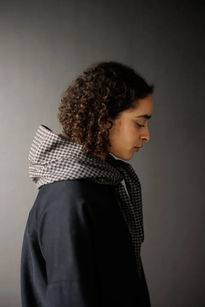 Woman wearing the Audrey Hooded Scarf sewing pattern from Merchant & Mills on The Fold Line. A scarf pattern made in mid-weight wool, double gauze, light to mid-weight corduroy and quilted jacquard fabrics, featuring a loose fitting lined hood with long t